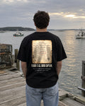 Rough Seas Ship's Log tee on a pier, back view