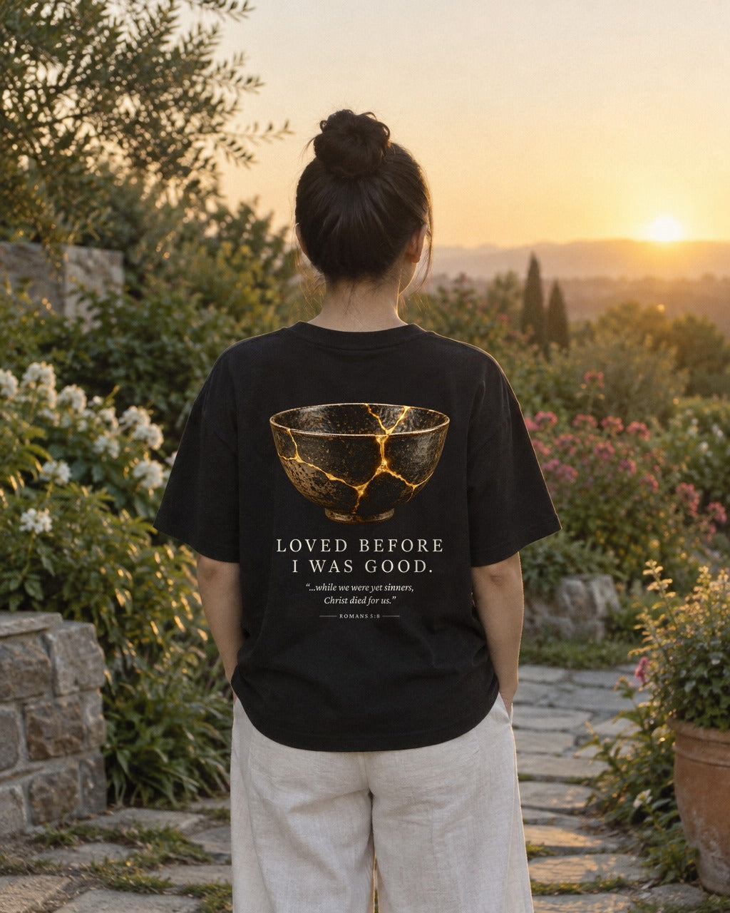 Loved Before I Was Good Kintsugi tee in a garden at sunrise, back view